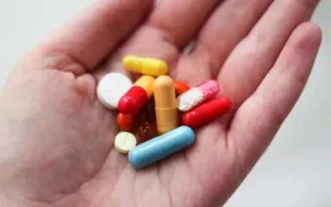 En hand håller flera färgglada piller och kapslar, inklusive en blå kapsel som kan vara en oxytocin tablett.