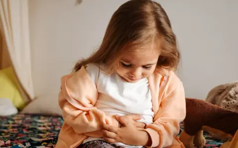 Liten flicka med händerna på magen, ser ut att ha diarre och illamående.