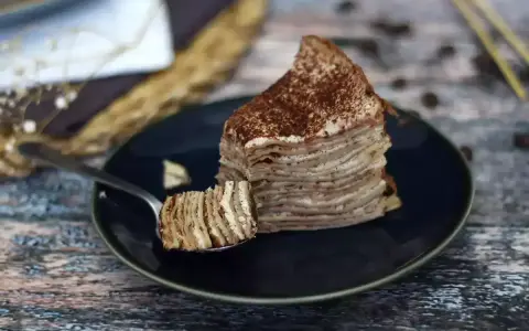 En skiva pannkakstårta med lager av grädde och kakao, perfekt för ett tiramisu recept.
