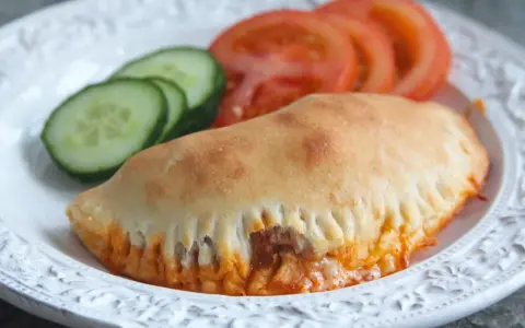 En gyllene pirog med ost och tomatsås, serverad med skivor av tomat och gurka. Ett perfekt piroger recept för en snabb och god måltid.