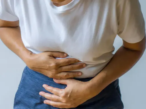 Person håller sig om magen, upplever smärta som kan vara relaterad till IBS och ont i ryggen.