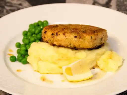 En gyllene havets wallenbergare serveras med krämigt potatismos, gröna ärtor och en citronskiva.