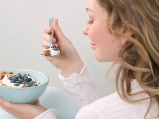 En kvinna äter en skål med yoghurt, blåbär och nötter. En hälsosam frukost som kan hjälpa till att få ner blodsockret.