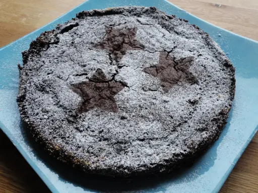 En härlig glutenfri kladdkaka med stjärnmönster av florsocker på en blå tallrik.