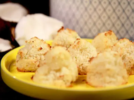 Små, gyllene kokostoppar på en gul tallrik, redo att avnjutas. Ett enkelt kokostoppar recept för hembakning.