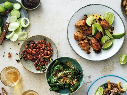 En härlig dukning med olika rätter av thai mat: kycklingvingar, friterade gröna paprikor, jordnötter och omogna mangos.