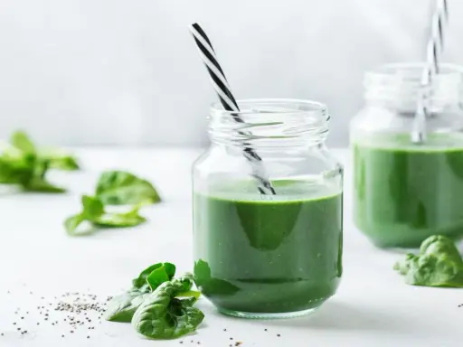 Två glas med grön smoothie, garnerade med färsk spenat och chiafrön. Tänk på spirulina biverkningar innan du dricker för mycket.
