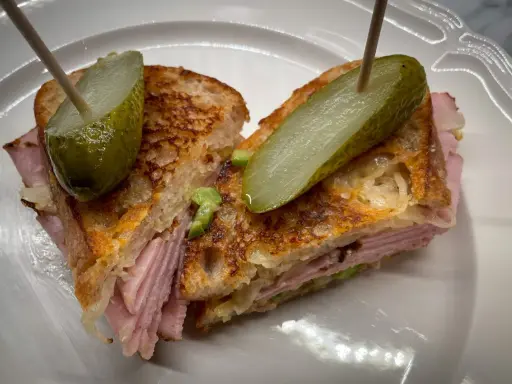 En saftig reuben sandwich med skinka, surkål och rostat bröd, toppad med dillgurka.