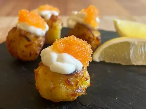 Små, krispiga tater tots toppade med gräddfil och orange rom. Citronklyftor ligger bredvid.