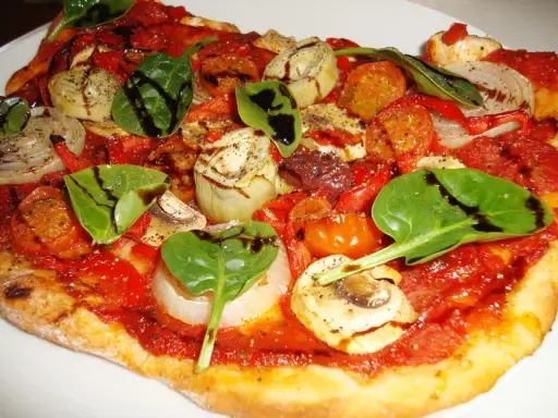 En läcker glutenfri pizza med tomatsås, grönsaker som lök, paprika, champinjoner, kronärtskocka och färsk spenat, toppad med balsamvinäger.