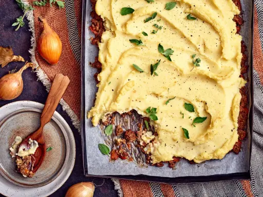 En ugnsbakad köttfärspaj med ett fluffigt potatismos som täcker hela ytan. Serveras med färska örter och peppar.