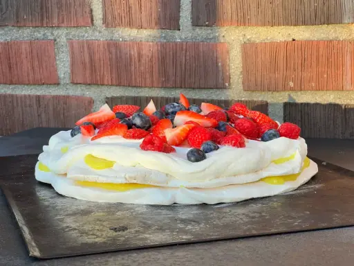 En vacker pavlova med lemoncurd, toppad med färska bär som jordgubbar, hallon och blåbär.