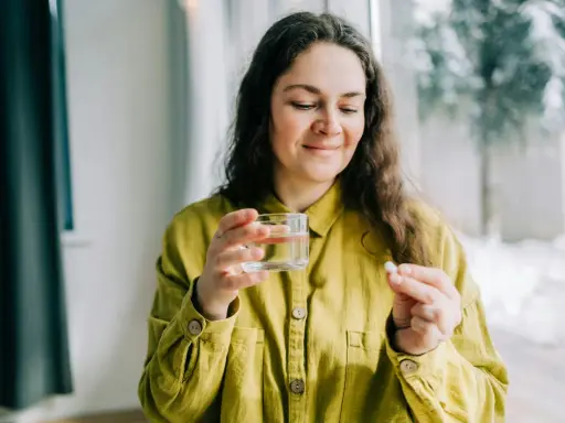 Kvinna med glas vatten och en tablett, funderar på magnesium tillskott biverkningar.