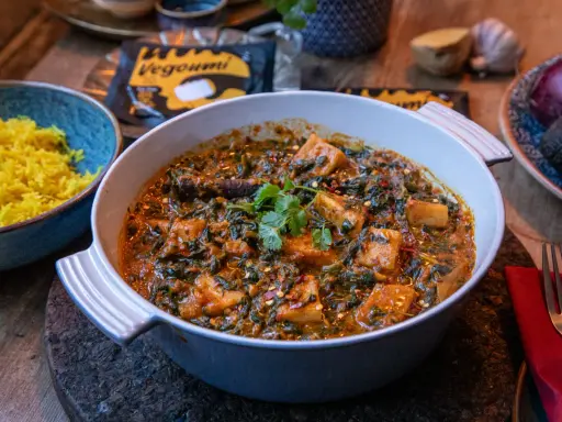 En krämig palak paneer med gyllene ris. Vegoumi-förpackning syns i bakgrunden.