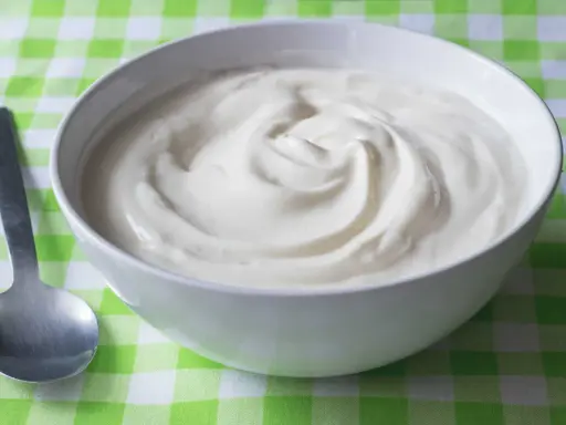 En skål med krämig yoghurt, redo att avnjutas. En sked ligger bredvid, perfekt för att ta en tugga av denna e 407-godhet.