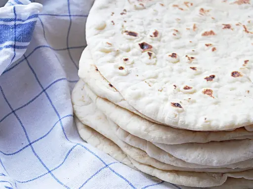 En hög med nybakade tortillas, perfekta för ditt nästa tortilla recept. En blårutig kökshandduk ligger bredvid.