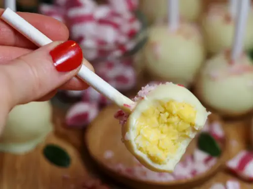 En hand med rött nagellack håller en cake pop. Den är doppad i vit choklad och strössel.