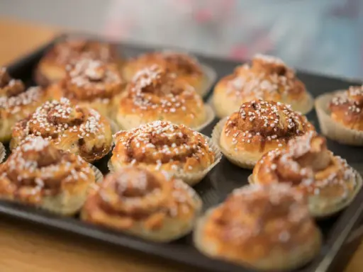 En plåt med nybakade glutenfria kanelbullar, toppade med pärlsocker. Doften av kanel sprider sig i köket.