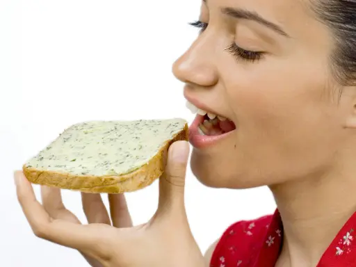 En kvinna med gluten mage njuter av en smörgås med örtsmör.