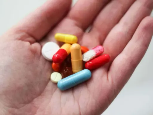 En hand håller flera färgglada piller och kapslar, inklusive en blå kapsel som kan vara en oxytocin tablett.