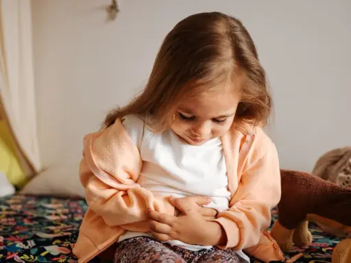 Liten flicka med händerna på magen, ser ut att ha diarre och illamående.
