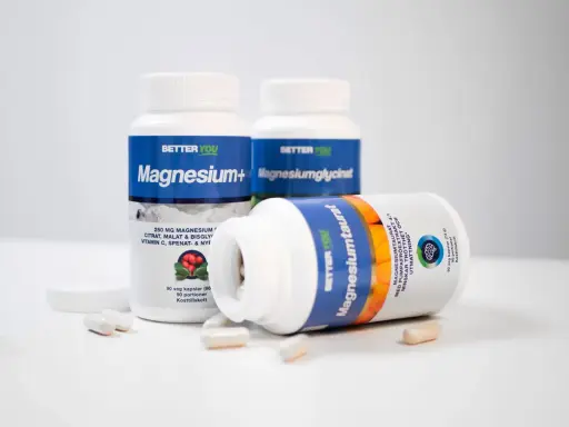 Tre burkar kosttillskott med magnesium. En burk ligger ner och visar texten "Magnesiumtaurat", som bidrar till att minska trötthet och utmattning, vilket är viktigt för magnesium i kroppen.