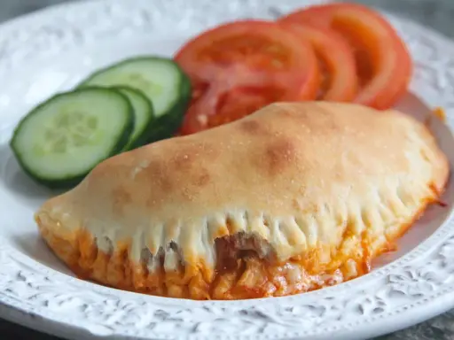 En gyllene pirog med ost och tomatsås, serverad med skivor av tomat och gurka. Ett perfekt piroger recept för en snabb och god måltid.