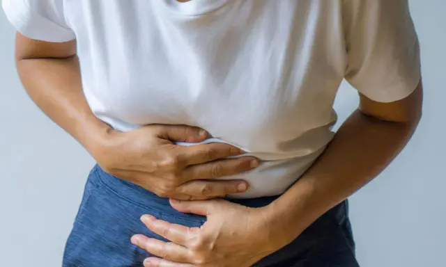 Person håller sig om magen, upplever smärta som kan vara relaterad till IBS och ont i ryggen.