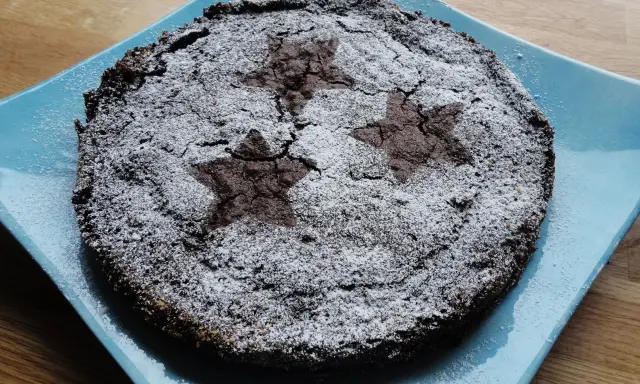 En härlig glutenfri kladdkaka med stjärnmönster av florsocker på en blå tallrik.