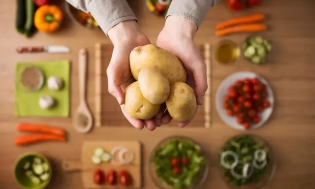 Händer håller färsk potatis, en del av en hälsosam måltid med grönsaker. Potatis nyttigt!