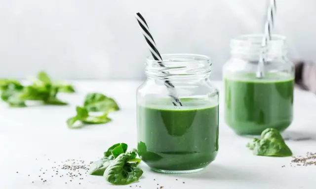 Två glas med grön smoothie, garnerade med färsk spenat och chiafrön. Tänk på spirulina biverkningar innan du dricker för mycket.