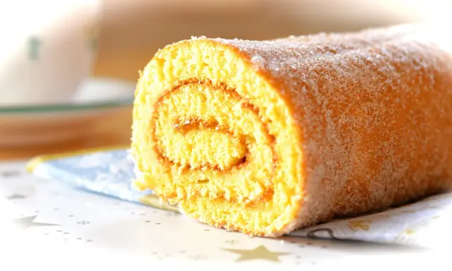 En saftig glutenfri rulltårta med socker strött över, perfekt för fikat.