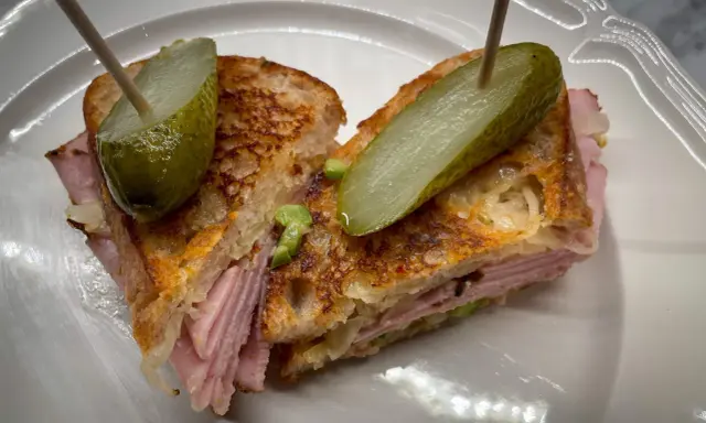 En saftig reuben sandwich med skinka, surkål och rostat bröd, toppad med dillgurka.