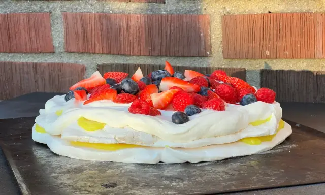 En vacker pavlova med lemoncurd, toppad med färska bär som jordgubbar, hallon och blåbär.