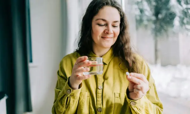 Kvinna med glas vatten och en tablett, funderar på magnesium tillskott biverkningar.