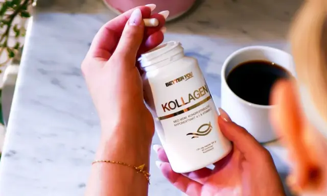 En hand håller en kapsel från en Better You Kollagen-burk. En kopp kaffe står bredvid. För en bättre du, natt biverkningar är minimala.