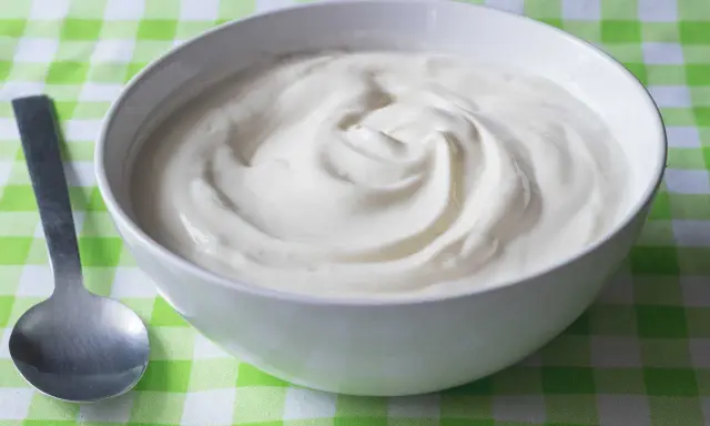 En skål med krämig yoghurt, redo att avnjutas. En sked ligger bredvid, perfekt för att ta en tugga av denna e 407-godhet.