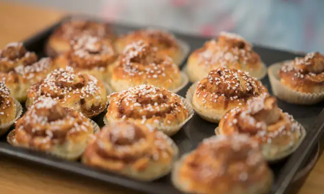 En plåt med nybakade glutenfria kanelbullar, toppade med pärlsocker. Doften av kanel sprider sig i köket.