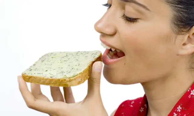 En kvinna med gluten mage njuter av en smörgås med örtsmör.