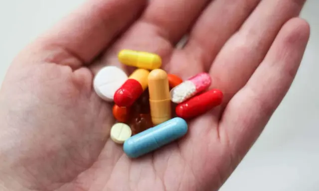 En hand håller flera färgglada piller och kapslar, inklusive en blå kapsel som kan vara en oxytocin tablett.