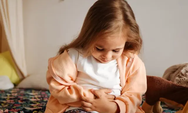 Liten flicka med händerna på magen, ser ut att ha diarre och illamående.