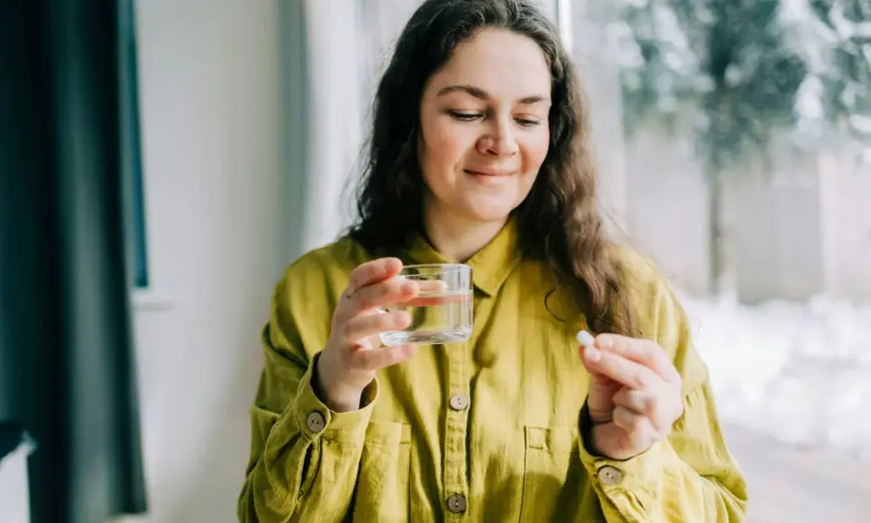 Kvinna med glas vatten och en tablett, funderar på magnesium tillskott biverkningar.