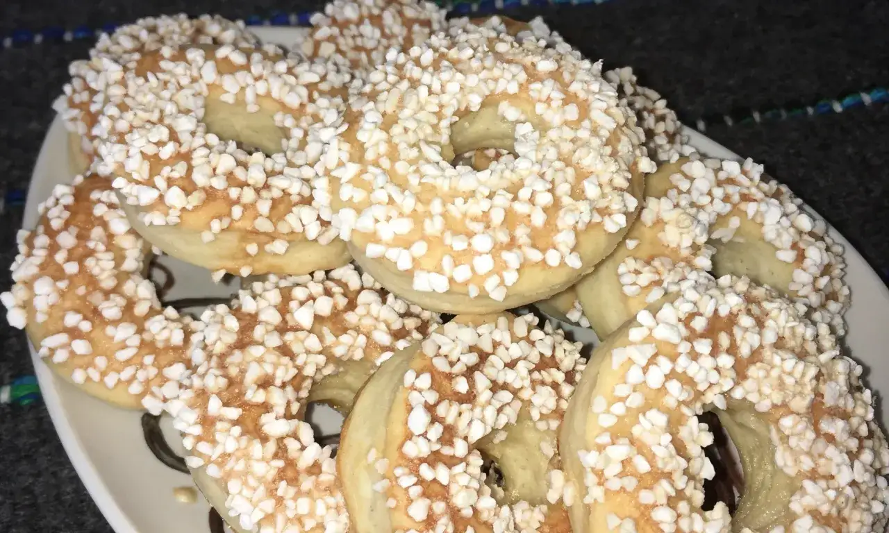 En h&ouml;g med gyllene finska pinnar, str&ouml;sslade med sockerp&auml;rlor, ligger p&aring; en vit tallrik.