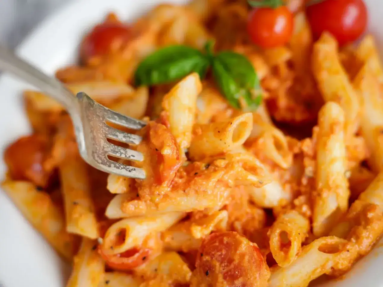 En gaffel lyfter en tugga av kr&auml;mig vodka pasta med k&ouml;rsb&auml;rstomater och basilika.