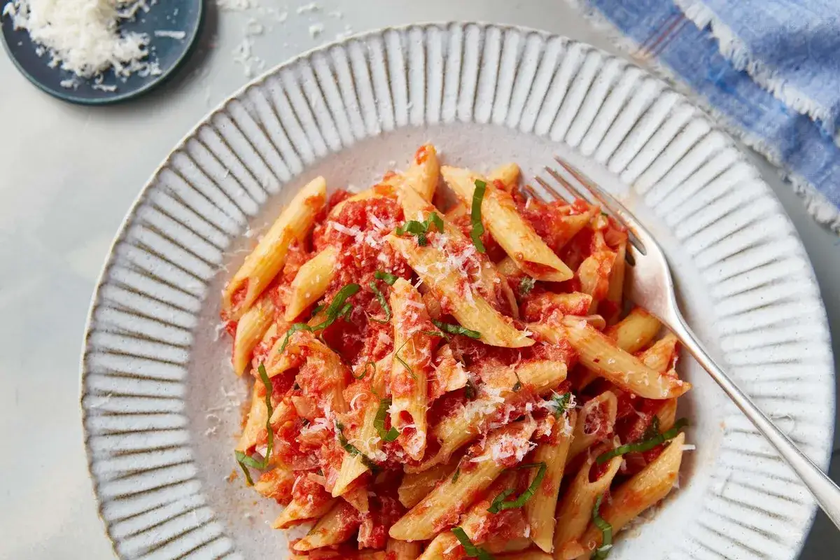 En tallrik med penne pasta arrabiata, toppad med riven parmesan och f&auml;rsk basilika. En gaffel ligger redo att avnjuta denna kryddiga italienska klassiker.