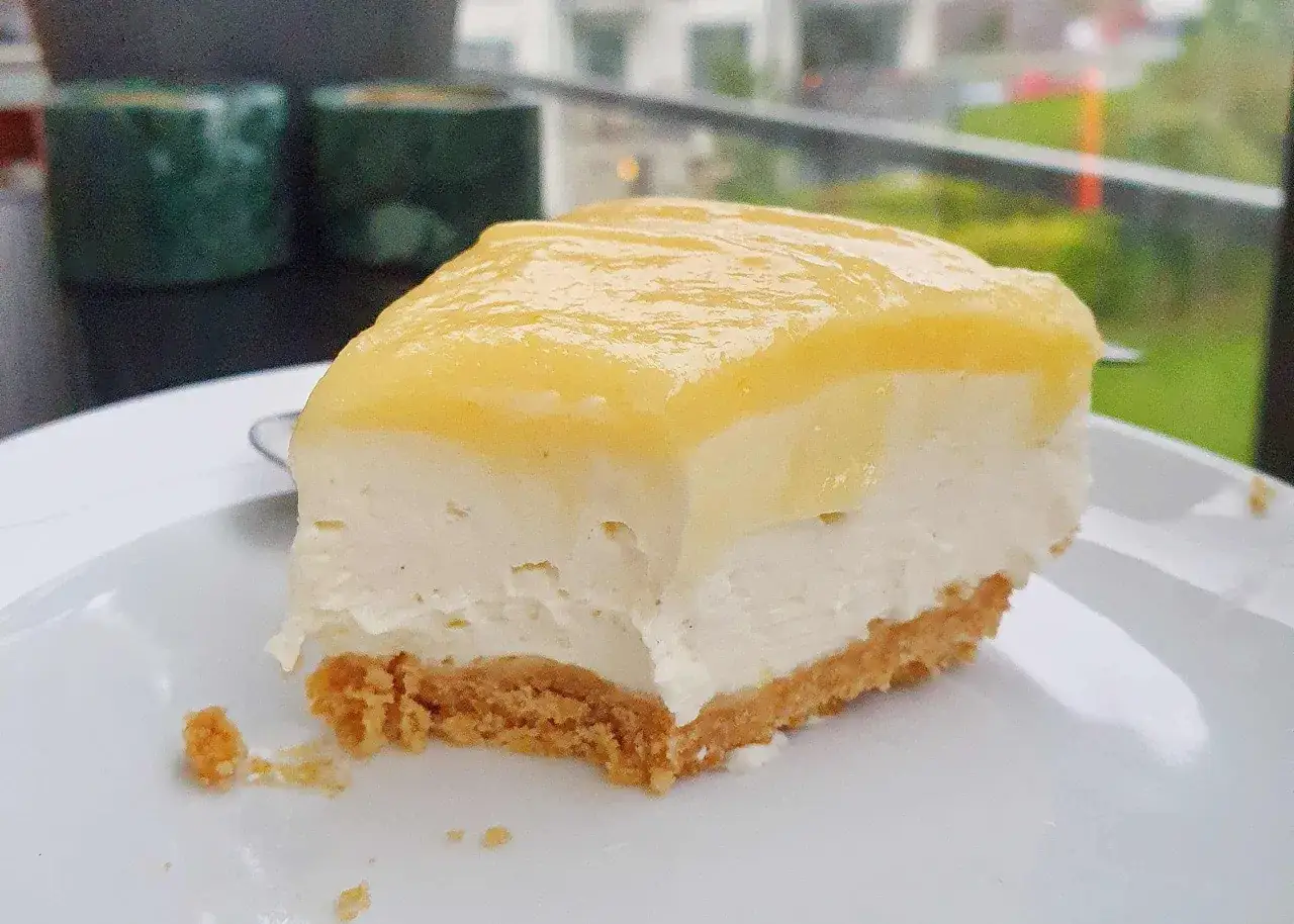 En bit kr&auml;mig cheesecake med gul topping p&aring; en vit tallrik. Perfekt f&ouml;r ett cheesecake recept.
