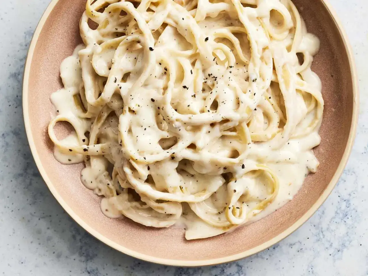 Kr&auml;mig pasta alfredo med svartpeppar p&aring; en ljusrosa tallrik.