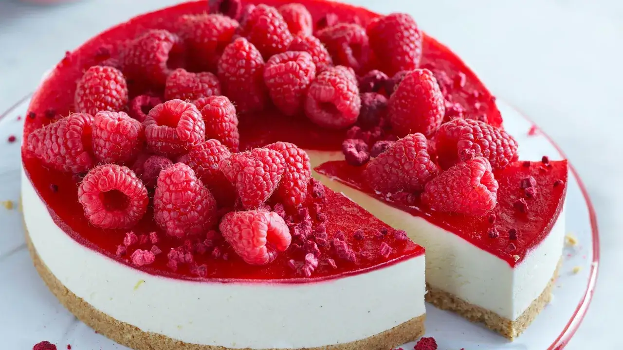 En kr&auml;mig cheesecake hallon med f&auml;rska b&auml;r och hallonspegel. En bit &auml;r uppskuren.