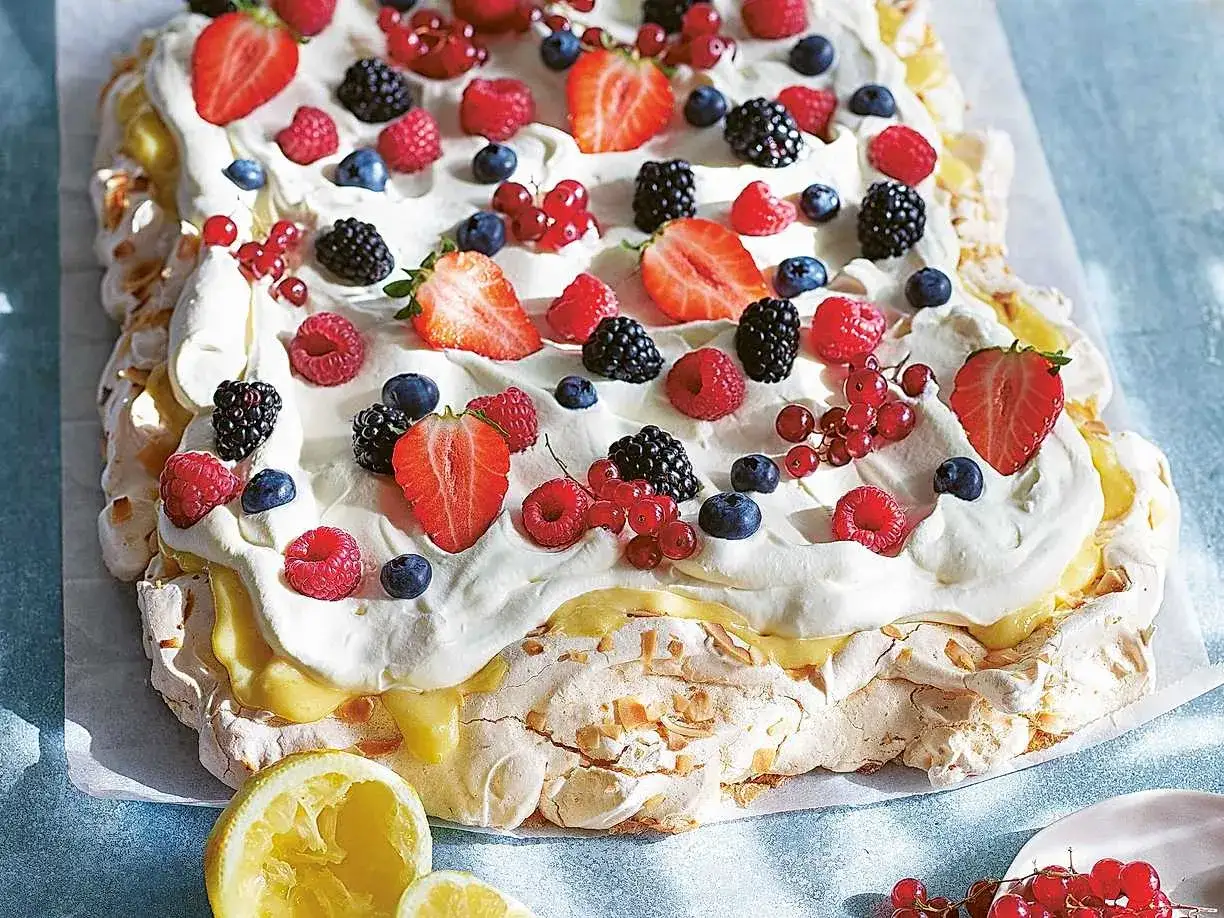 En stor pavlova med lemoncurd, toppad med vispgr&auml;dde och f&auml;rska b&auml;r som jordgubbar, hallon, bl&aring;b&auml;r och vinb&auml;r.