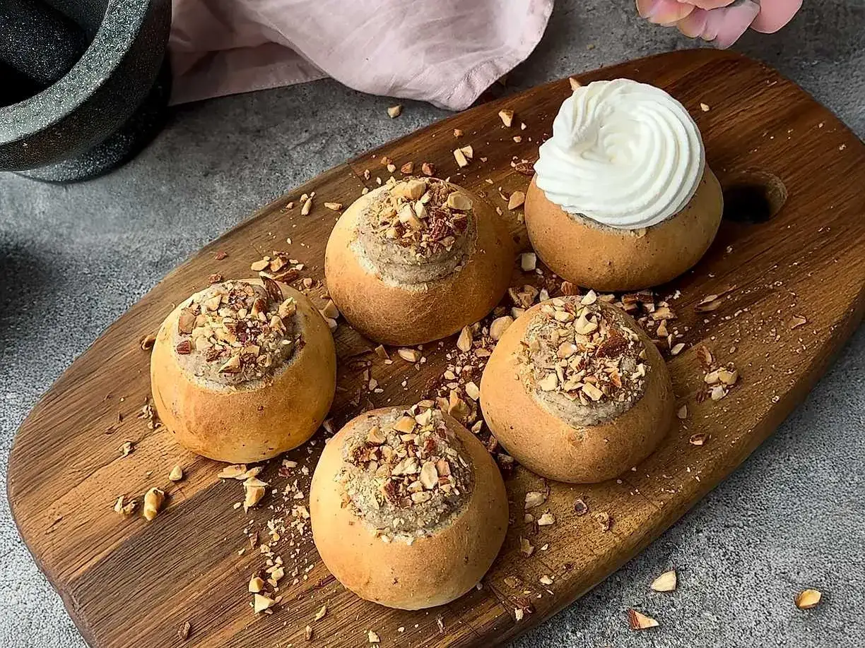 Fem nybakade semlor på ett träfat, fyllda med härlig mandelmassa till semlor och toppade med hackade nötter. En är dekorerad med vispgrädde.